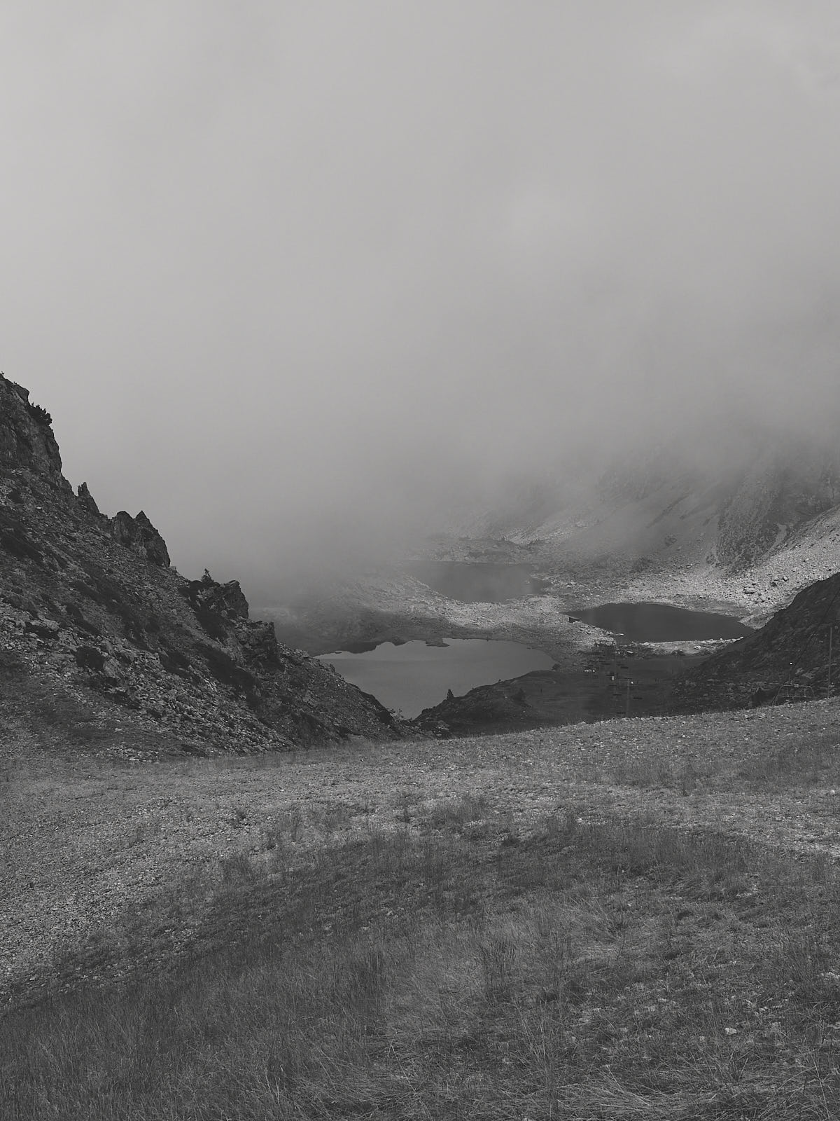 Black and white valley with three small lakes fading into the fog
