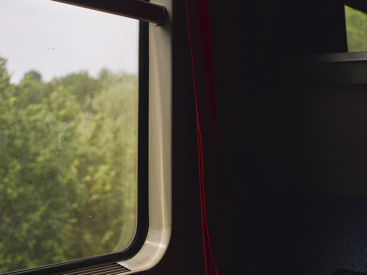 Close-up of a train window and a red curtain, soft light coming from outside