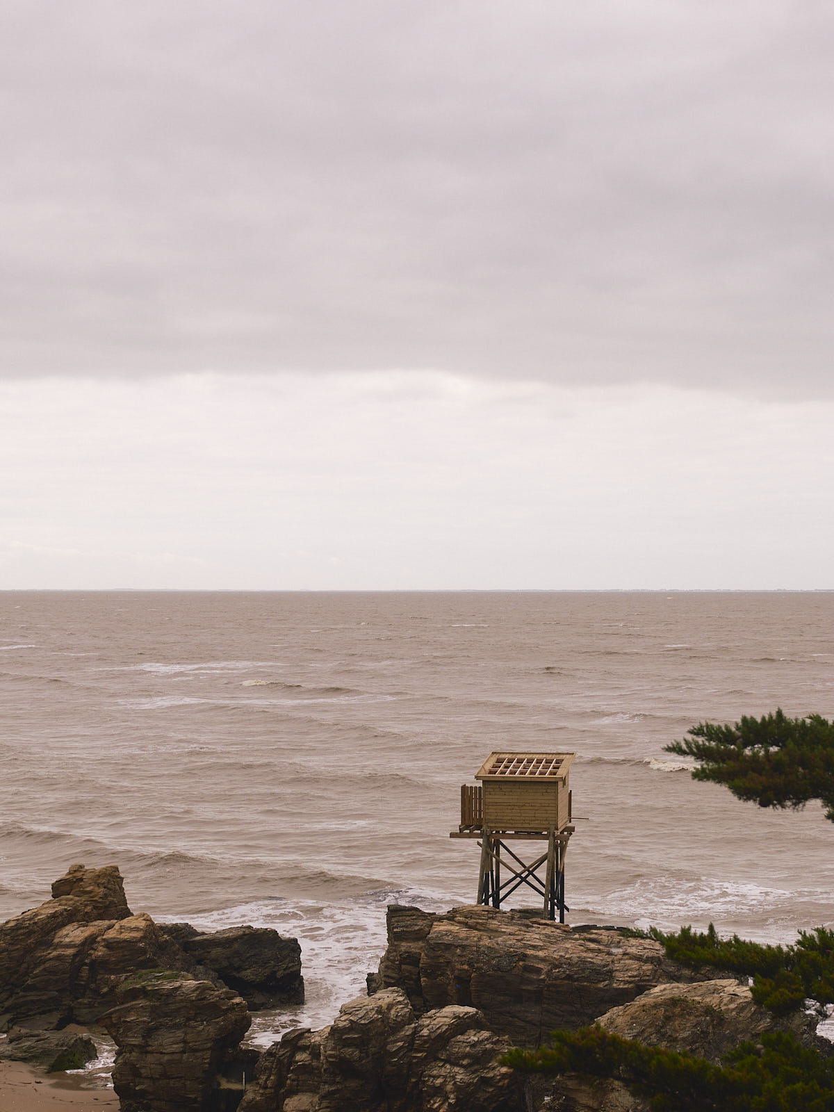 Wooden fishing shed perched atop rocks, next to the ocean