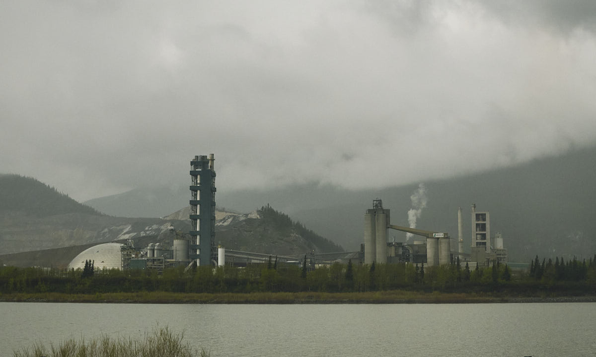 Industrial complex right in front of a lake, with cloudy mountains behind