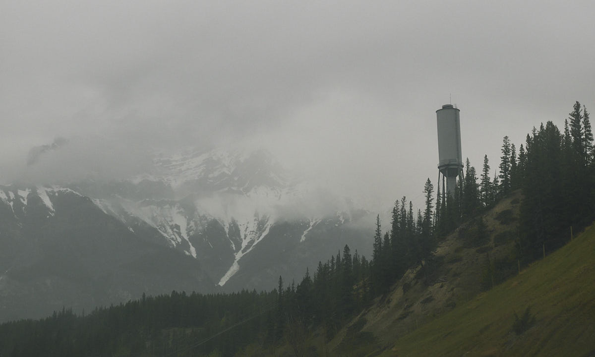 Water tower on the side of a hill, with trees lining up along the slope and a foggy background
